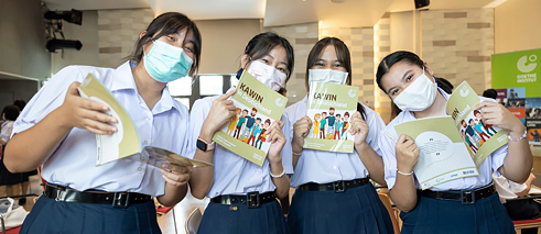 นักเรียนหญิงสี่คนกำลังอ่านหนังสือ "กวินในเยอรมนี" และยิ้มให้กล้อง