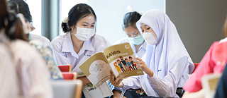 Two schoolgirls look together into the book “Kawin in Germany”.
