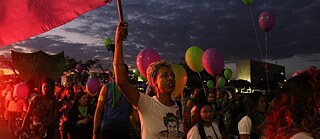 Woman holding red flag; in background crowd with balloons