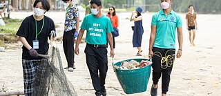 Menschen heben Müll vom Strand auf und sammeln ihn in großen Körben.