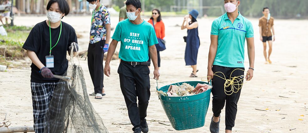 People pick up trash from the beach and collect it in large baskets.