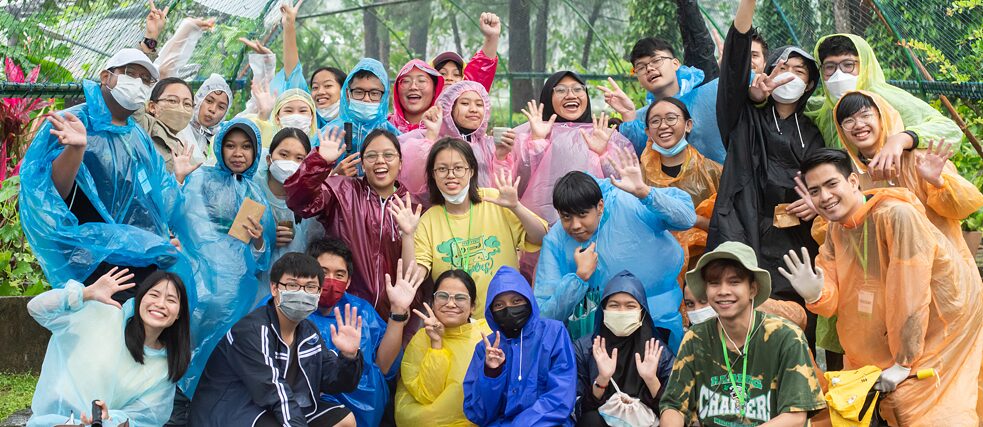 Eine Gruppe junger Menschen steht in der Natur und winkt in die Kamera.