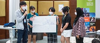 Fünf Personen halten ein A1-Blatt mit einer Grafik hoch und erklären sie.