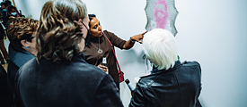 Three women looking at an artwork on the wall, one woman is pointing at it and explaining something