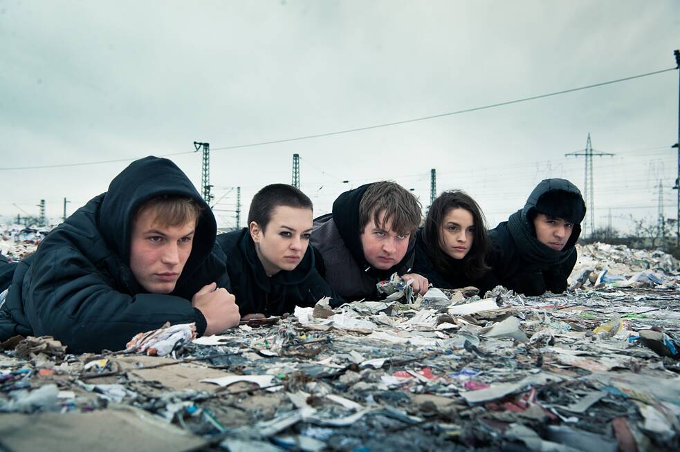 Still da série alemã original da Netflix Nós somos a onda: um grupo de cinco adolescentes espreita em cima de fardos de papel descartado