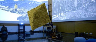 Screening of next...II (Mali/Iceland) at the Nordic House Reykjavík projected on three walls in the screening room. In the foreground a diamond shape is seemingly floating in the picture, overgrown with moss.