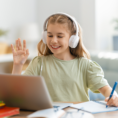 Girl with headphones waving and smiling at a laptop