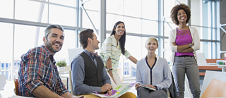 Besprechung in einem Büro. Die Personen lächeln und sind begeistert. Ein Mann blickt in die Kamera.