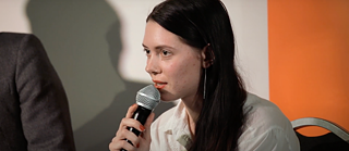 Three men with glasses, the one in the middle speaks into the microphone.
