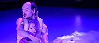 Kaksi toisiinsa kietoutunutta ihmistä violetissa valossa