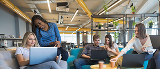 Group of coworkers sitting on sofas with laptops during an online Business German course in a collaborative workspace.