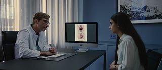 Eine junge Frau sitzt bei einem Gynäkologen im Besprechungsraum.