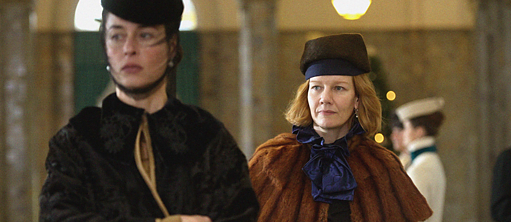 Dos mujeres noblemente vestidas atraviesan un vestíbulo.