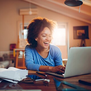 Eine Frau lacht beim Lernen vor ihrem Computer.