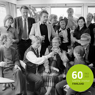 Mustavalkoinen kuva, jossa iso porukka kilistää kuohuviinilaseja