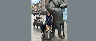 Narmawarni Abdul Kadir sitzt auf einen Brunnen in einer Fußgängerzone und lacht.