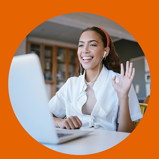 Eine lächelnde Schülerin mit Kopfhöreren winkt in die Kamera ihres Laptops