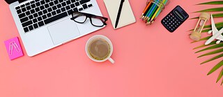Aufnahme von oben auf einen Schreibtisch mit Notizzetteln, Brille, Stift und Tastatur.