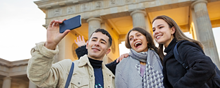 Três pessoas jovens tiram uma selfie em frente ao Brandenburger Tor