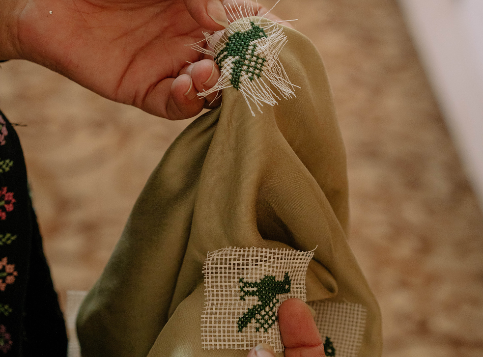 Dalal zeigt zwei Vögel, die sie auf einen Schal gestickt hat. Die weißen Fäden werden am Ende entfernt. 