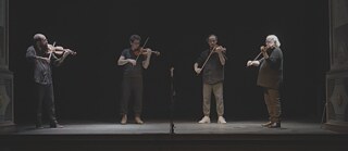 Quatro homens num palco jogam violino 