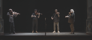 Quatro homens num palco jogam violino 
