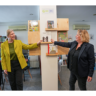 Zwei hochrangige Frauen legen gemeinsam ein Buch in ein Regal der deutsch-französischen Pop-up-Bibliothek 