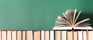 Bücher stehen aufgereiht mit der offenen Seite zum Betrachter. Obenauf liegt ein aufgeblättertes Buch.