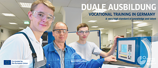 Zwei Jungen nehmen an einer Lernaktivität in einer Firma teil. Sie stehen an einer Maschine und lernen die Bedienung kennen. 