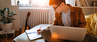 Ein Jugendlicher sitzt auf dem Bett und lernt Deutsch online.