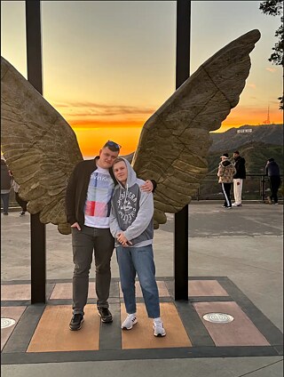 Max and Dmitrii in front of a sculpture of oversized wings, with the iconic Hollywood sign in the background.