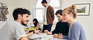 Eine Gruppe fröhlicher Menschen lernt zusammen, der Lehrer betreut die Lernenden. 