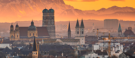 Blick auf die Skyline Münchens mit der Frauenkirche zu Sonnenuntergang. Alpenpanorama im Hintergrund.