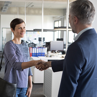 Two professionals shaking hands in an office environment, symbolizing a successful business meeting or agreement.