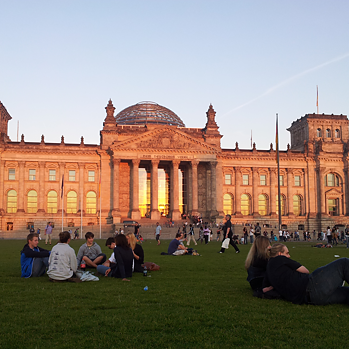 Das Reichstagsgebäude in Berlin mit Menschen, die sich auf dem Rasen niedergelassen haben.