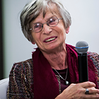 Małgorzata Łukasiewicz, eine Dame mit grauem Kurzhaarschnitt und Brille, lächelt, während sie ein Mikrofon hält.