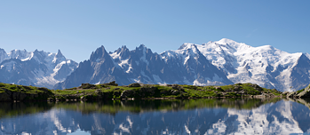 Bergpanorama, dass sich bei strahlendem Sonnenschein in einem See spiegelt.