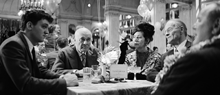 Fünf Personen sitzen an einem Tisch bei einem festlichen Tanzabend, umgeben von Ballons und Dekorationen.