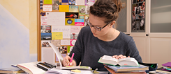 Une jeune femme travaille ses exercices de préparation à l'examen 'Goethe Zertifikat'. Elle est assise à son bureau, la tête penchée sur ses livres.