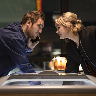 Ein Mädchen und ein Junge starren sich an, während sie etwas aus dem Kühlschrank eines Geschäfts nehmen. 