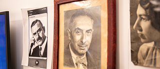 Drei Fotografien, nebeneinander an einer Wand hängend: links ein ausgedruckter Screenshot eines Thomas Mann-Posters, auf dem Mann in Denker Pose nach rechts schaut. In der Mitte ein Portraitbild von Michael Sieders Vater, daneben ein Portraitfoto seiner Mutter. Alle Bilder in schwarz-weiß.