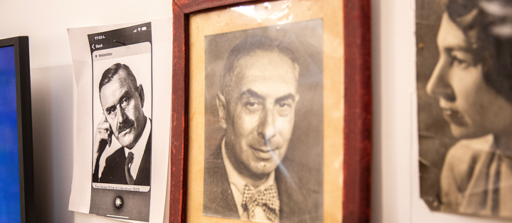 Три фотографії висять поруч на стіні: ліворуч - роздрукований скріншот плаката з Томасом Манном, на якому Манн дивиться направо у позі мислителя. У центрі - портрет батька Міхаеля Зідера, поруч - портрет його матері. Усі зображення чорно-білі.