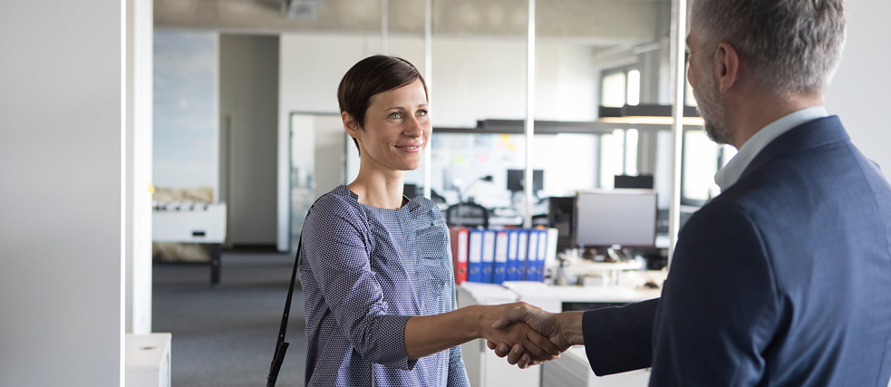 Two professionals shaking hands in an office environment, symbolizing a successful business meeting or agreement.
