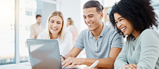 Zwei Frauen und ein Mann sitzen lächelnd vor einem Laptop