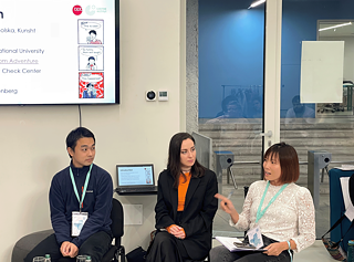 An assembly of people sits in chairs in front of a screen and is focused on the content of the presentation.