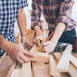 Werkbank mit Holz, wo zwei Personen ein Holz vermessen