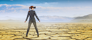 Mujer adulta en traje con lentes de realidad virtual parada en un desierto.