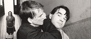 A blond young man and an older dark-haird man fight with each other