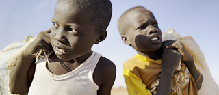 Zwei Jungen stehen zusammen in einer weiten Wüstenlandschaft unter einem strahlend blauen Himmel. Es handelt sich um die Straßenjungen Street boys Lokain and Wilson, die Flaschen sammeln.