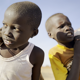 Two young boys stand together in a vast desert landscape under a clear blue sky. Street boys Lokain and Wilson collecting bottles.
